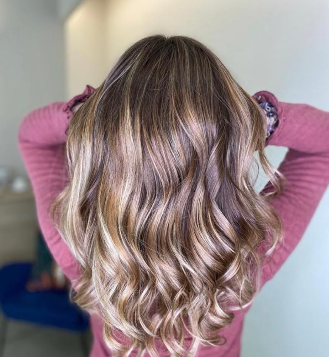 Melena castaña con ondas y reflejos claros sobre top rosa