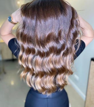 Melena castaña con ondas y reflejos cobrizos, brazos hacia arriba