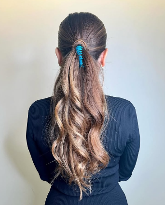 Coleta baja castaña con ondas y liga azul decorativa, vista de espalda